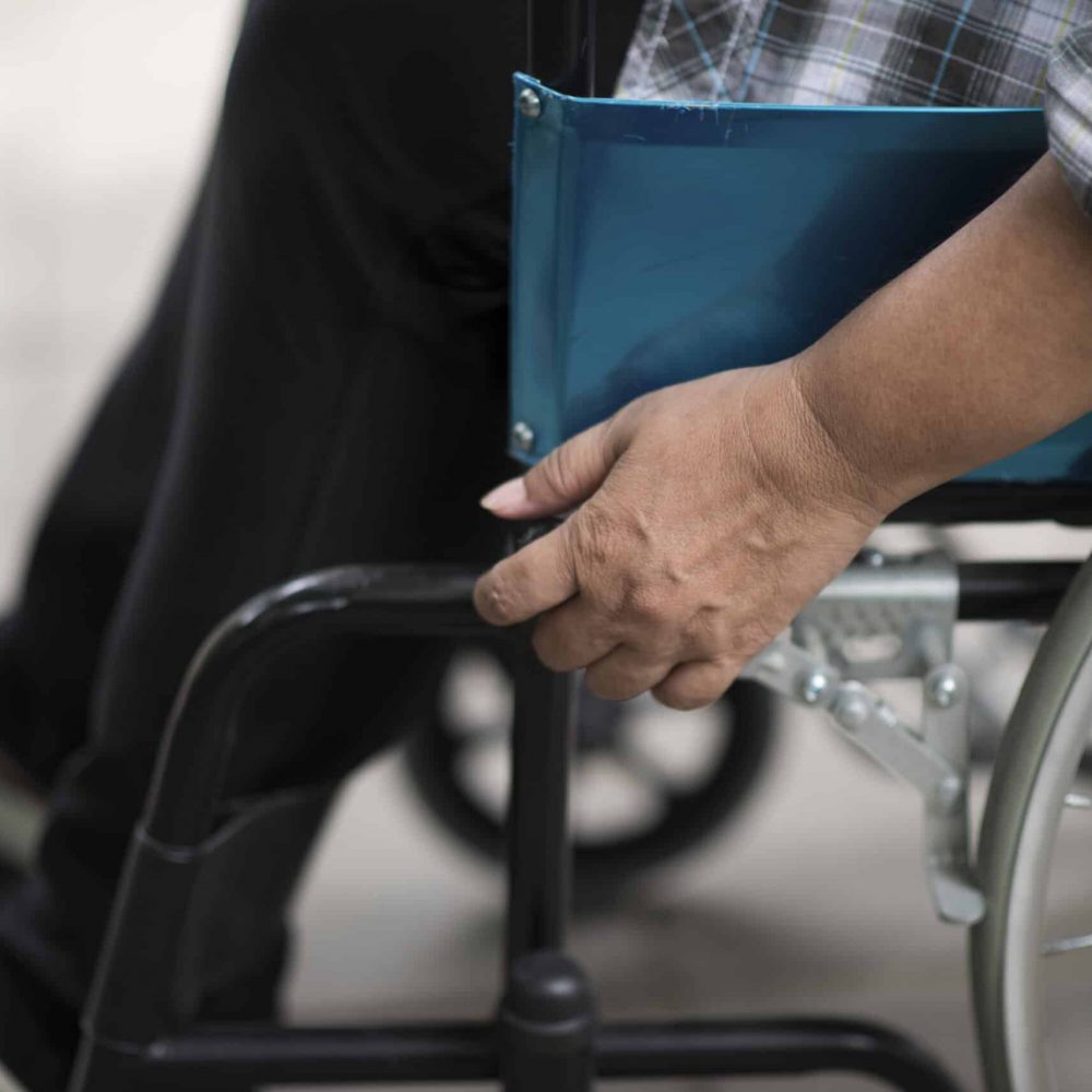 Close-up of senior woman hand on wheel of wheelchair during walk in hospital